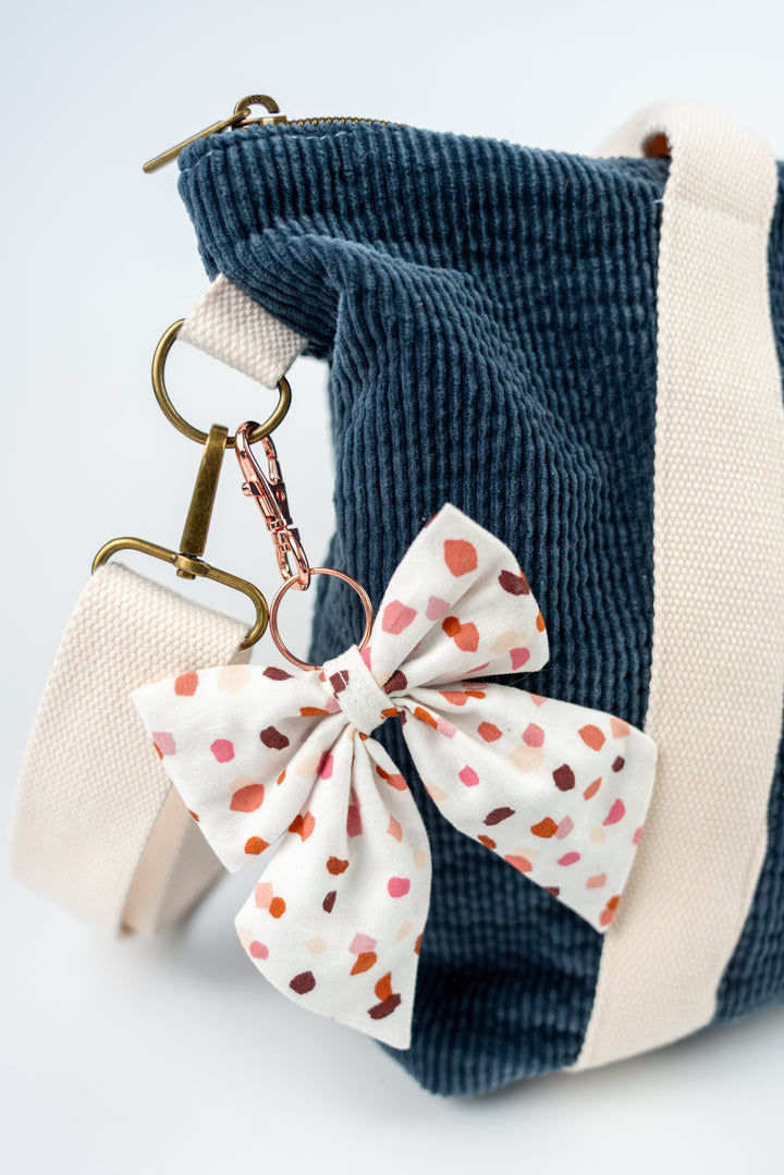 Bow keychain with polka dots attached to a blue corduroy bag on a white background