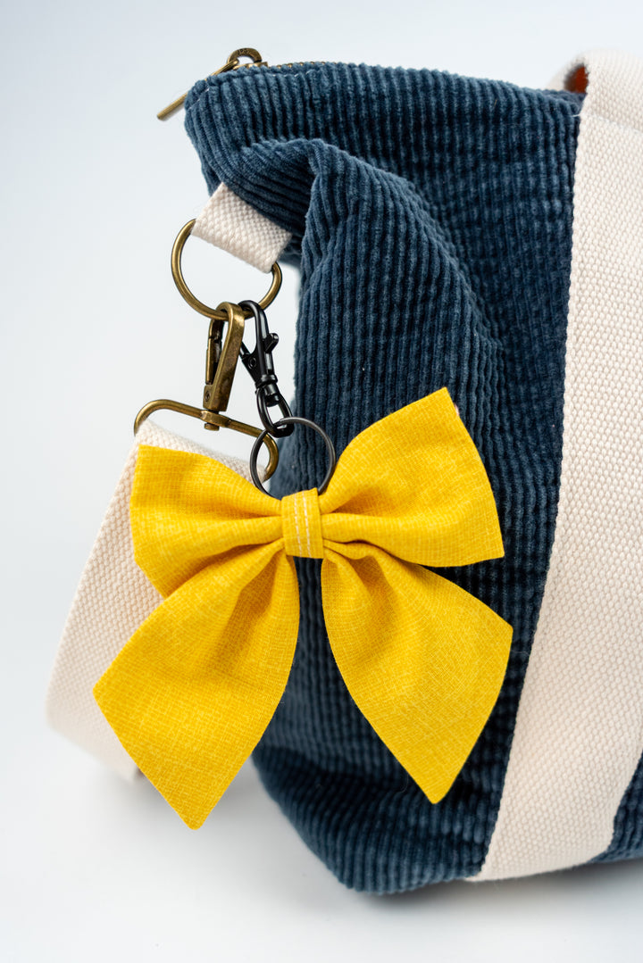 Blue corduroy bag with a yellow bow keychainon a white background