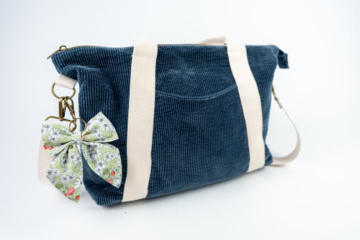 Blue corduroy bag with a floral keychain on a white background
