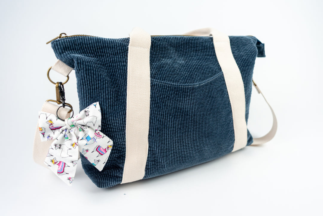 Blue corduroy bag with a decorative bow keychain on a white background