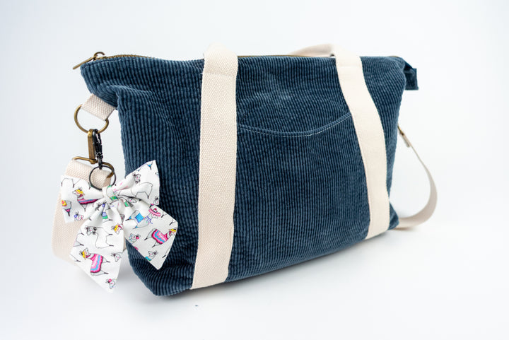Blue corduroy bag with a decorative bow keychain on a white background