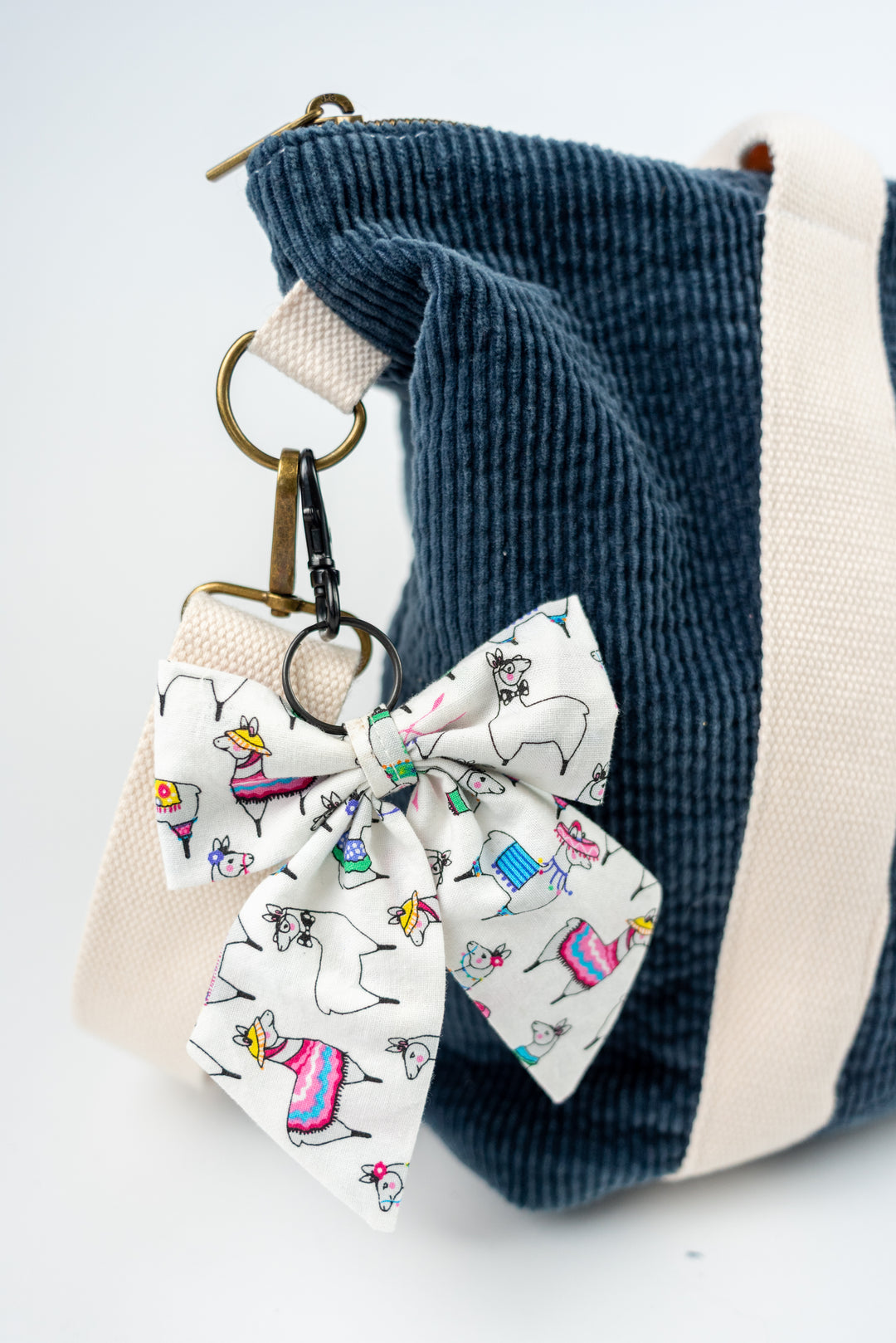 Bow keychain with llamas attached to a blue corduroy bag on a white background