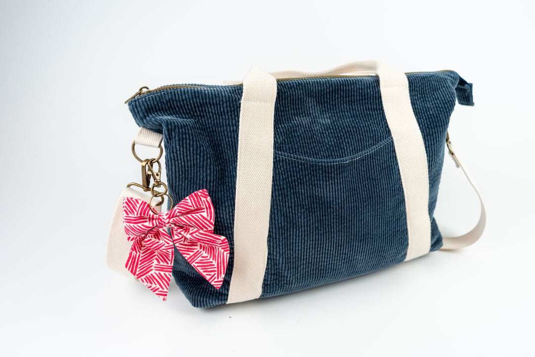 Blue corduroy bag with a pink bow keychain on a white background