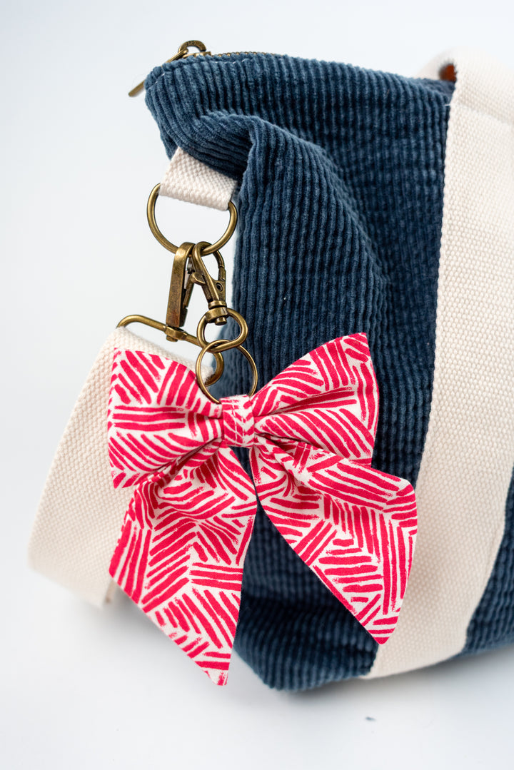 Keychain with a pink bow attached to a blue corduroy bag on a white background