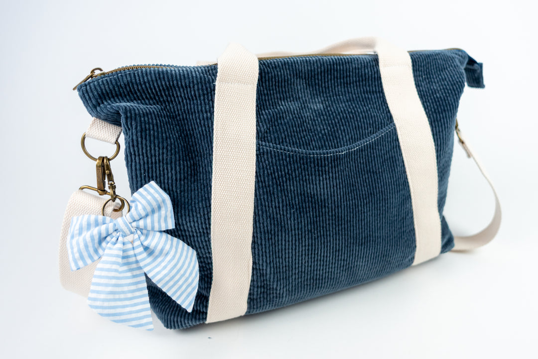 Blue corduroy bag with a white strap and a blue and white striped bow keychain on a white background