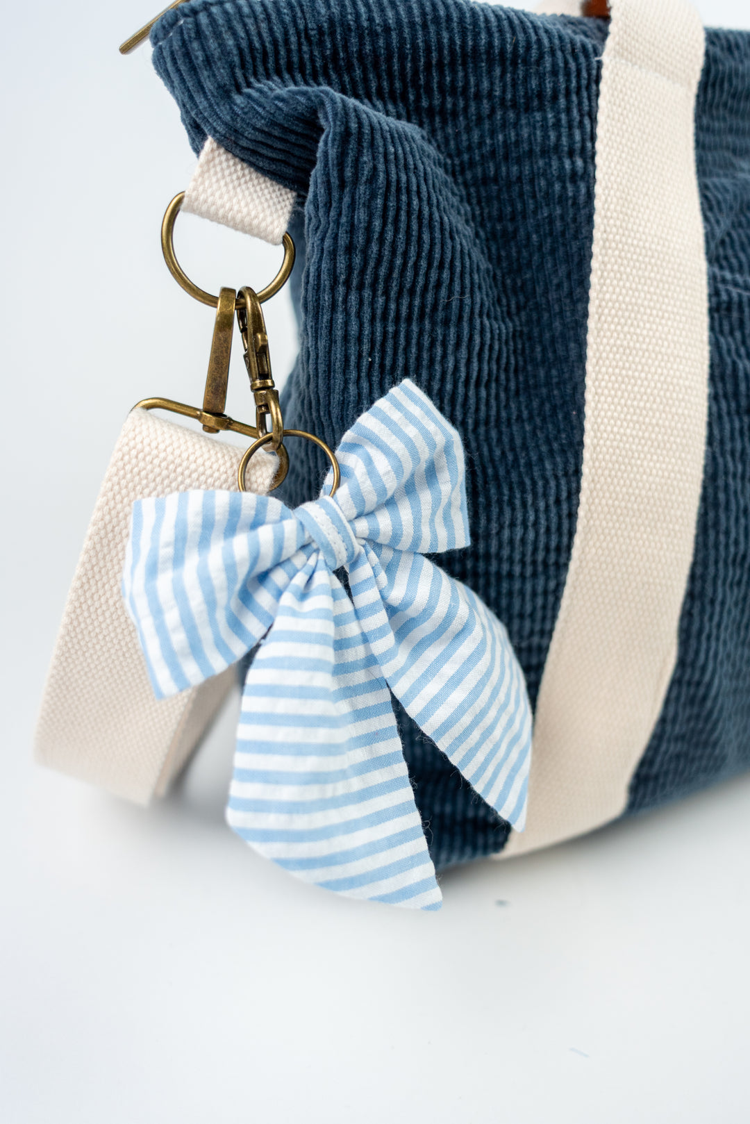 Blue corduroy bag with a keychain featuring a blue and white striped bow on a light background