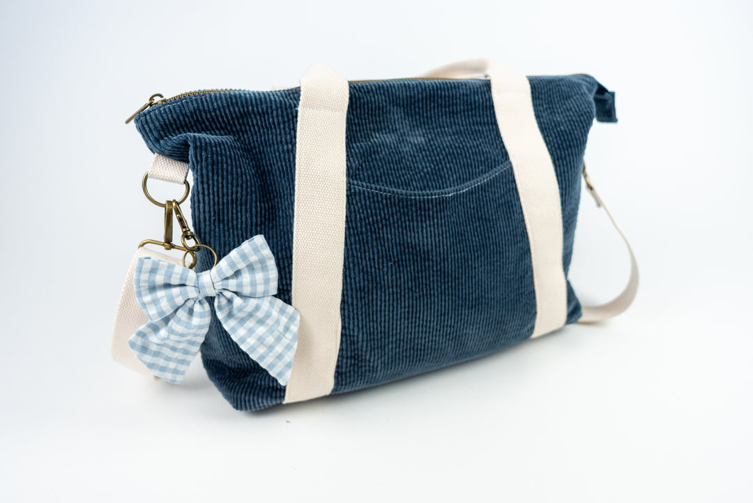 Blue corduroy bag with a bow keychain on a white background