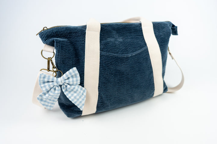 Blue corduroy bag with a bow keychain on a white background