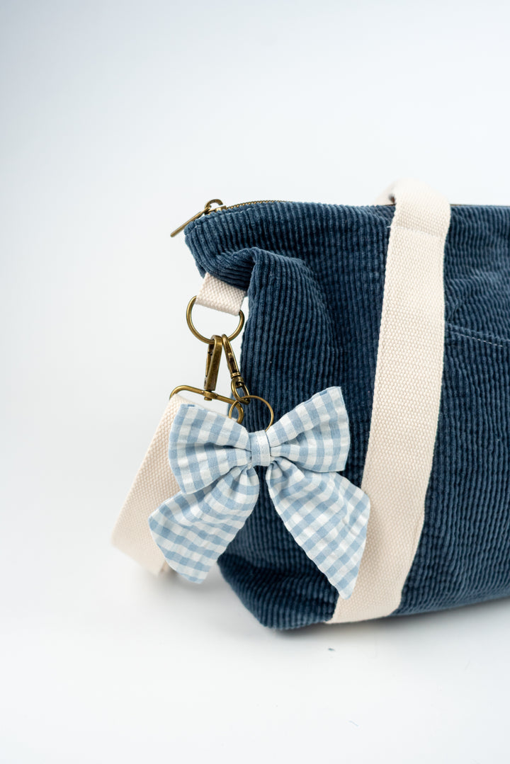 Blue corduroy bag with a checkered bow and keychain on a white background