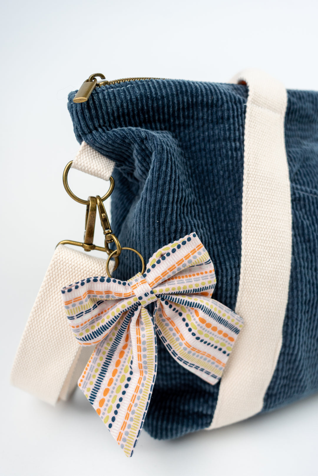 Blue corduroy bag with a striped bow keychain on a white background