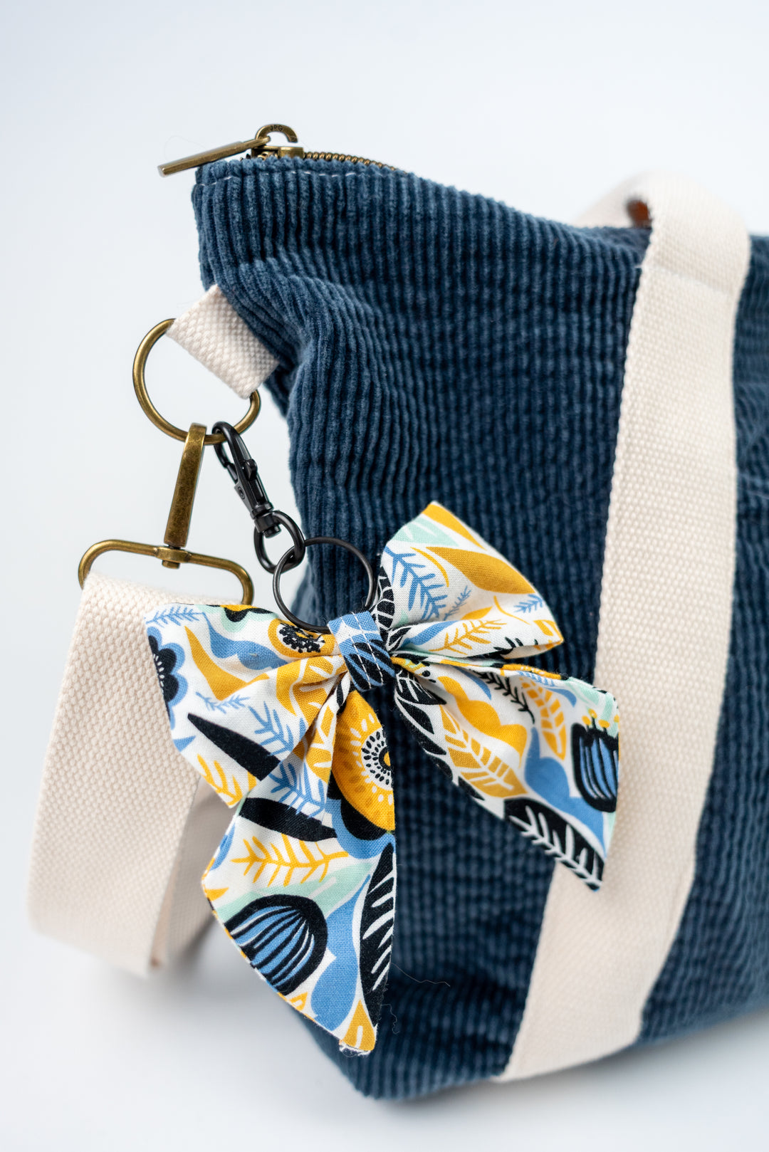 Blue corduroy bag with a bow keychain featuring a yellow and blue pattern on a white background