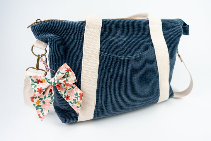 Blue corduroy bag with floral bow keychain on a white background