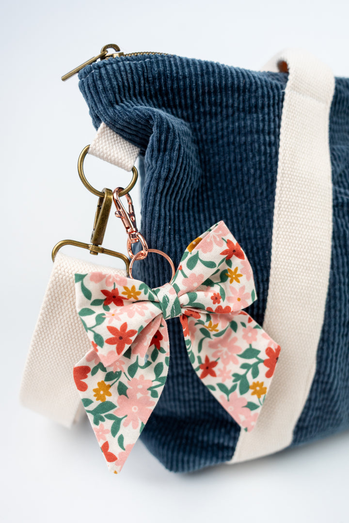 Floral keychain attached to a blue corduroy bag on a light background